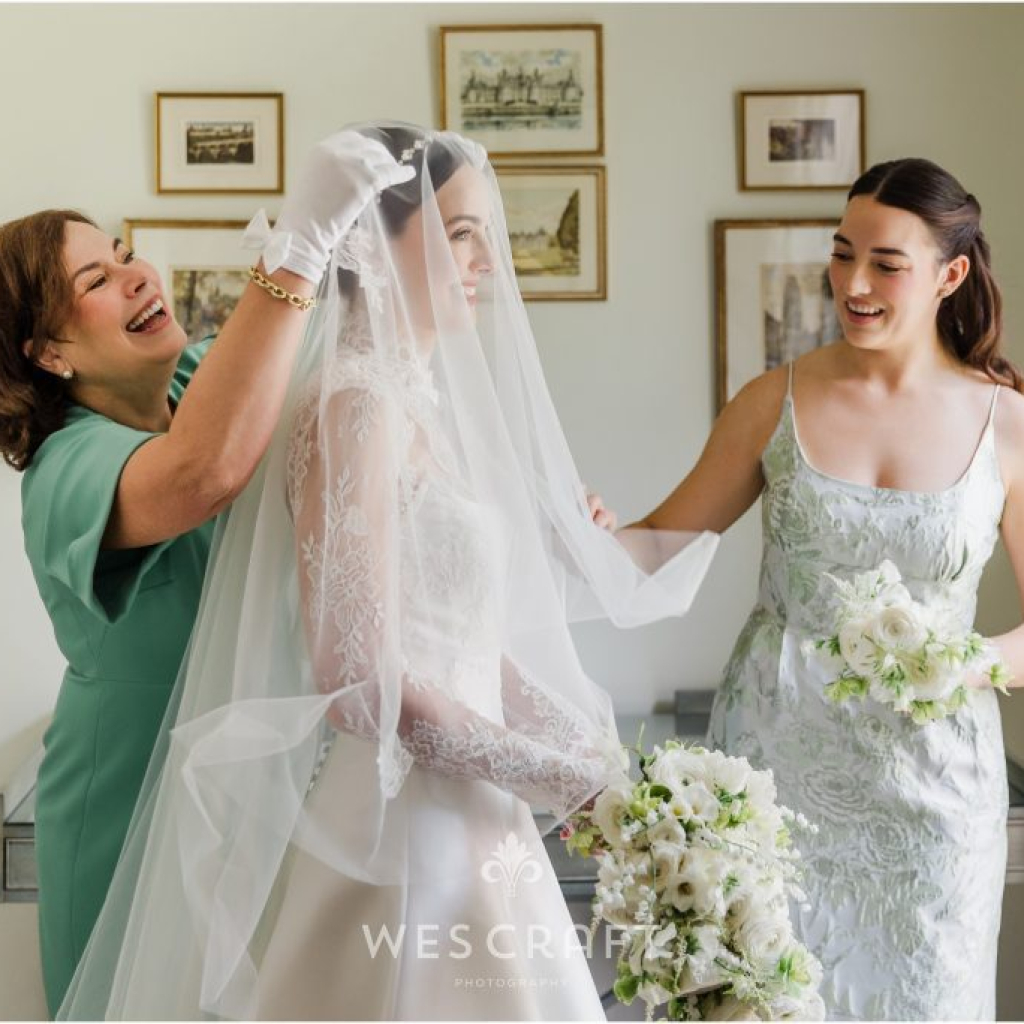 Mother adjusts her daughter's veil as bride's sister helps.